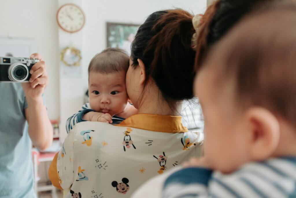 A mother holding her baby while taking a mirror selfie indoors.
