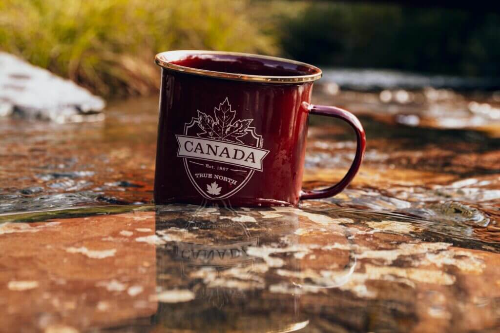 Red metal mug with Canada design placed in a river setting during fall.