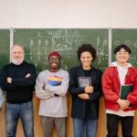 A diverse group of students and a teacher smiling in front of a chalkboard filled with formulas.